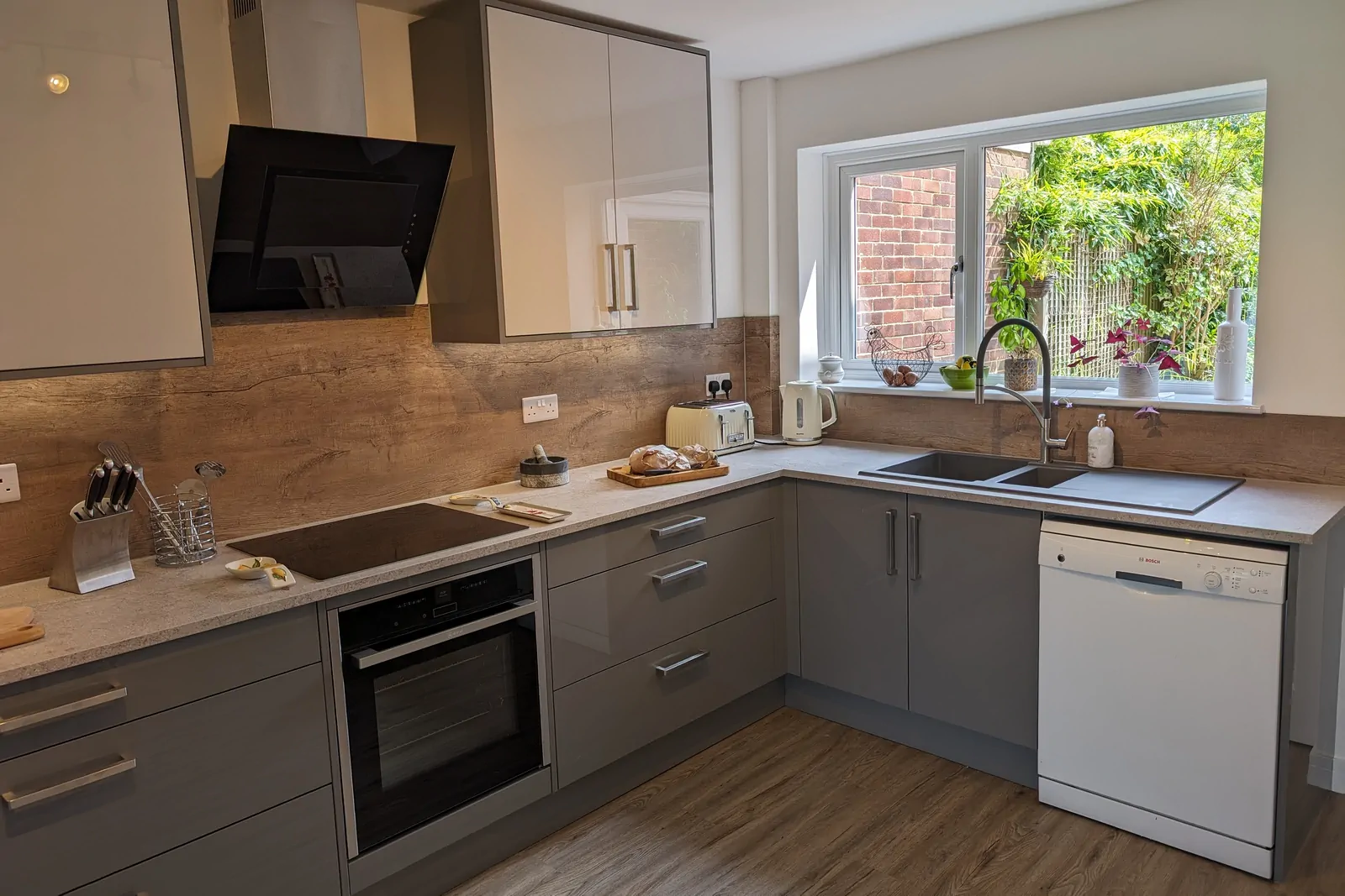 Induction hob with angled extractor opposite the double bowl sink, surrounded by continuous Calais Travertine worktops and oak-effect splashback for efficient working.