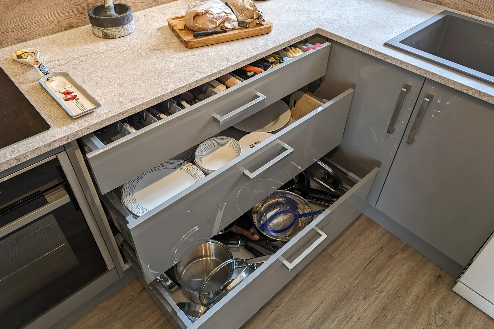 Set of wide, soft-close pan drawers open to show loads of organised cutlery, crockery, and cookware storage.