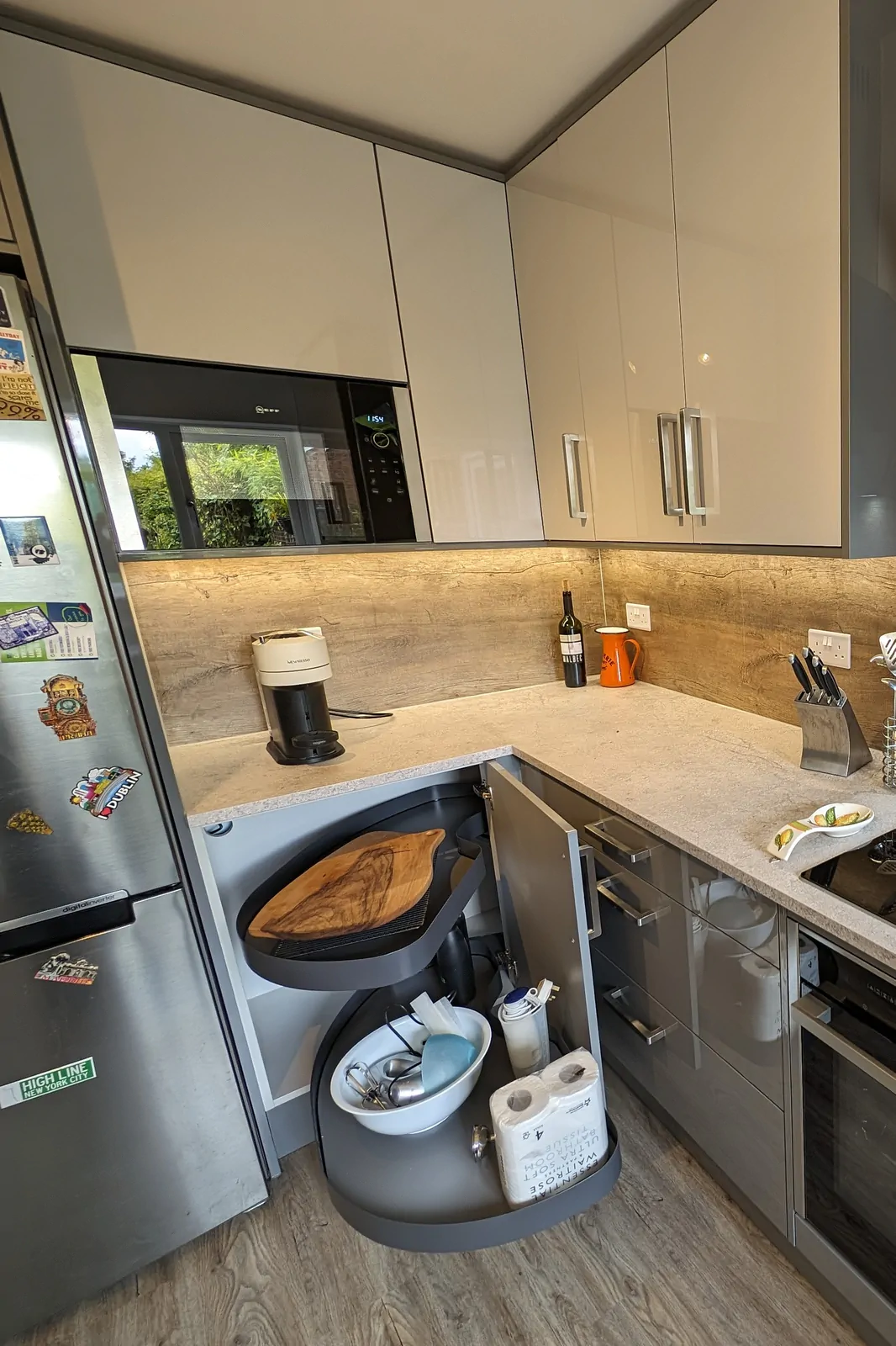 Corner base unit with twin pull-out trays in a gloss Dust Grey kitchen with Calais Travertine laminate worktop and oak-effect splashback.