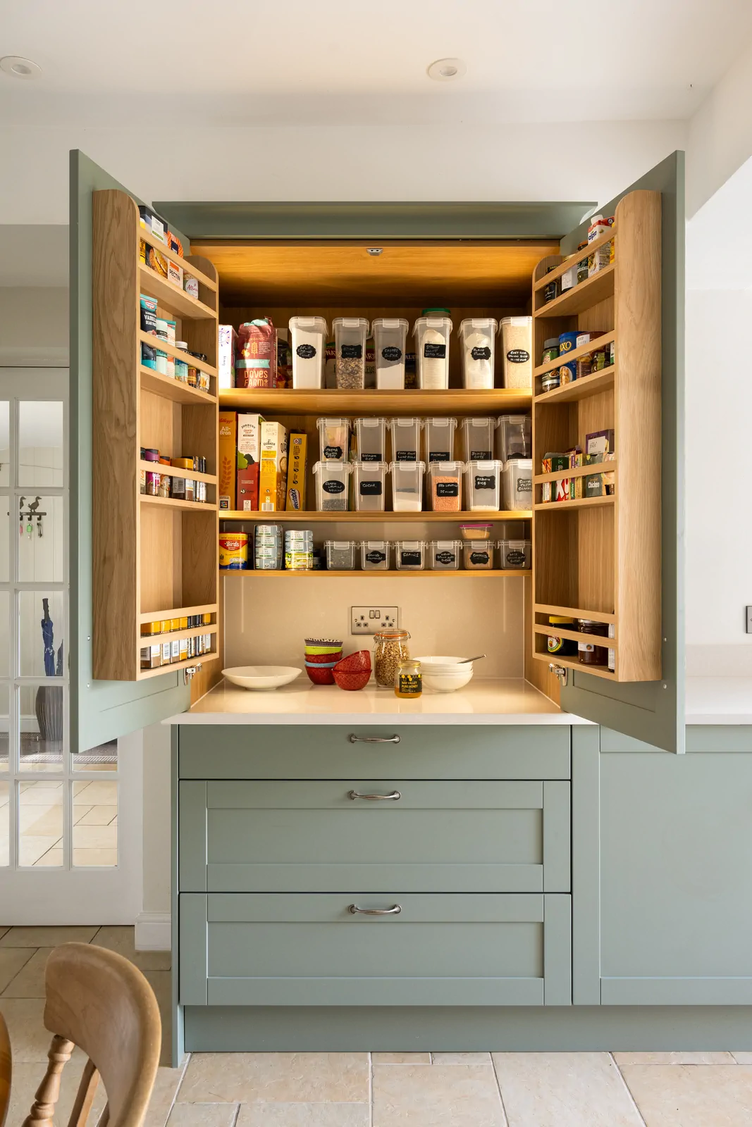 Oak interior pantry cabinet in a reed green shaker kitchen by Redwood Kitchens, Wokingham – illuminated and neatly organised with labelled containers.