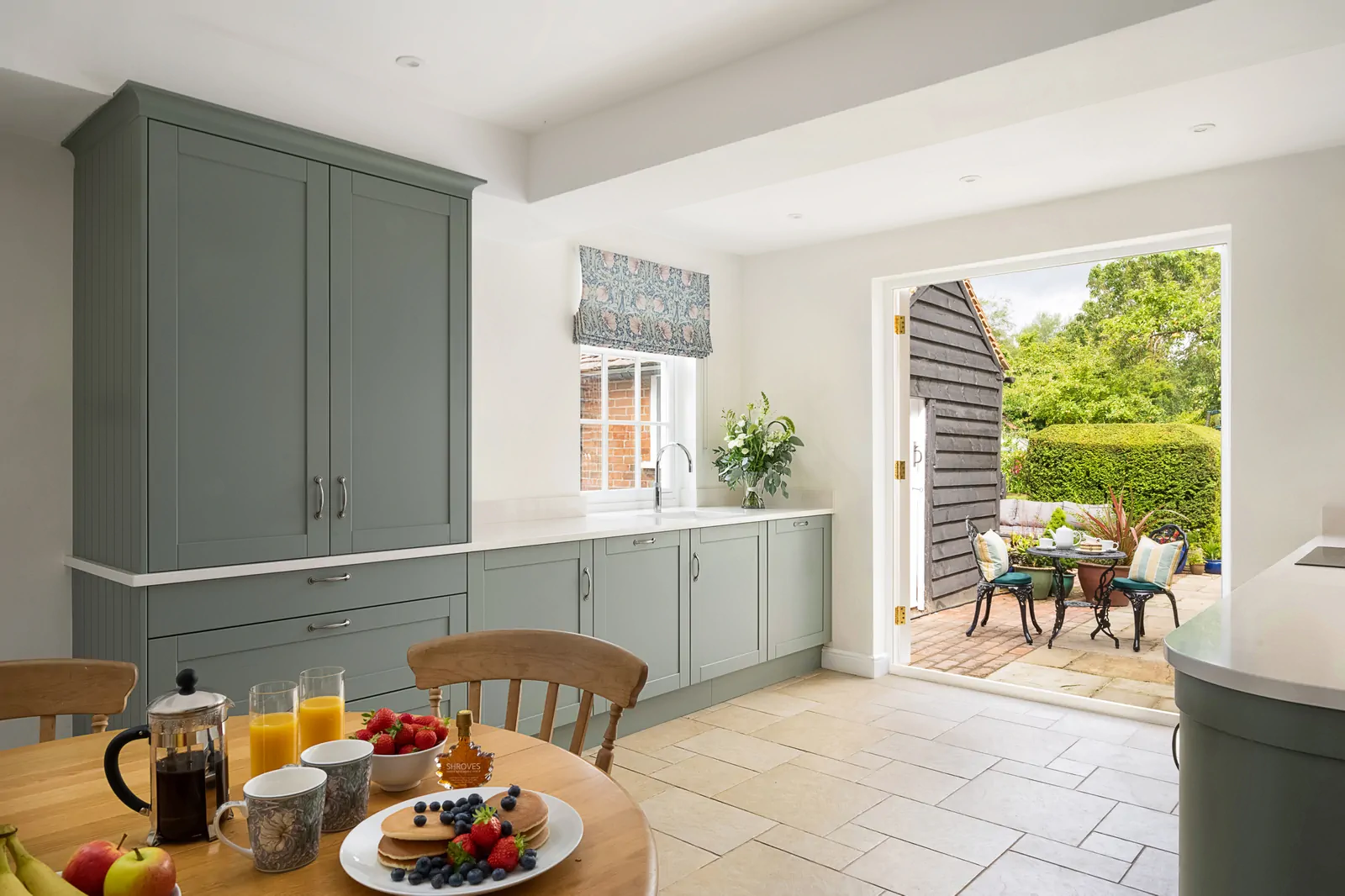 Reed green shaker kitchen in Binfield with undermount sink, Quooker boiling tap, Silestone quartz worktops, and breakfast table looking out to a patio garden. Designed and installed by Redwood Kitchens, Wokingham.
